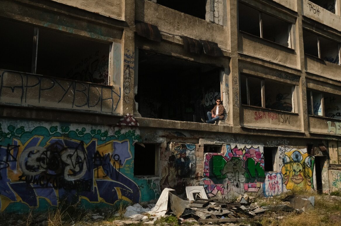 Karol Majcher siedzący w oknie opuszczonego budynku pokrytego graffiti